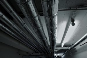 Mehrere gedämmte Heizungsrohre einer Deckenheizung verlaufen parallel unter der Kellerdecke in einem Technikraum.