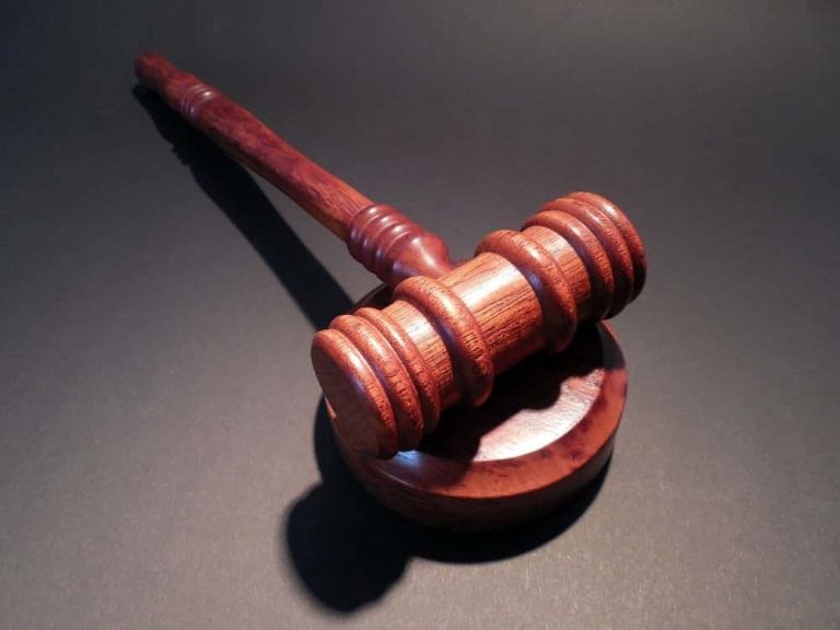 Ein hölzerner Richterhammer liegt auf einem dunklen Untergrund. Der Hammer hat ein detailliertes, poliertes Finish und ist ein Symbol für Recht und Justiz. Das Licht betont die Maserung des Holzes und erzeugt Schatten.