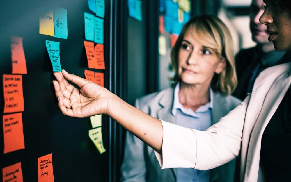 Mann erklärt Frau etwas mithilfe von Post-its an einer Wand
