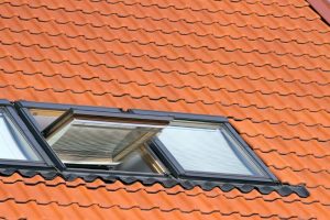 Geöffnetes modernes Dachfenster mit integrierter Jalousie in einem roten Ziegeldach an einem sonnigen Tag.