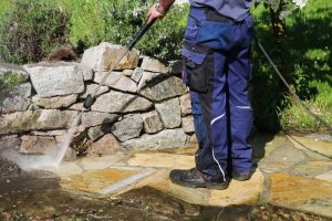 Gartenbauer entfernt mit Hochdruckreiniger Moos von einer Naturstein-Terrasse im Garten.