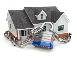 Symbolisches Modellhaus, das mit einer schweren Metallkette und einem Vorhängeschloss gesichert ist – Darstellung von Haussicherheit, Eigentumsschutz oder Immobilienversicherung.