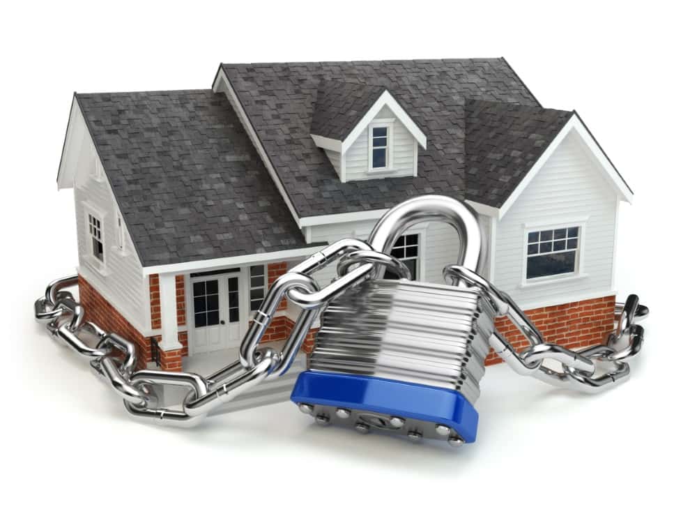 Symbolisches Modellhaus, das mit einer schweren Metallkette und einem Vorhängeschloss gesichert ist – Darstellung von Haussicherheit, Eigentumsschutz oder Immobilienversicherung.