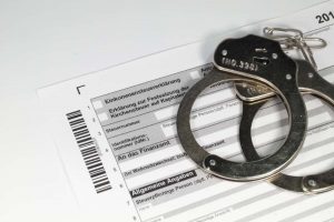 Handschellen liegen auf einer Einkommensteuererklärung – symbolisiert Konsequenzen bei Steuerhinterziehung und die Möglichkeit einer strafbefreienden Selbstanzeige.