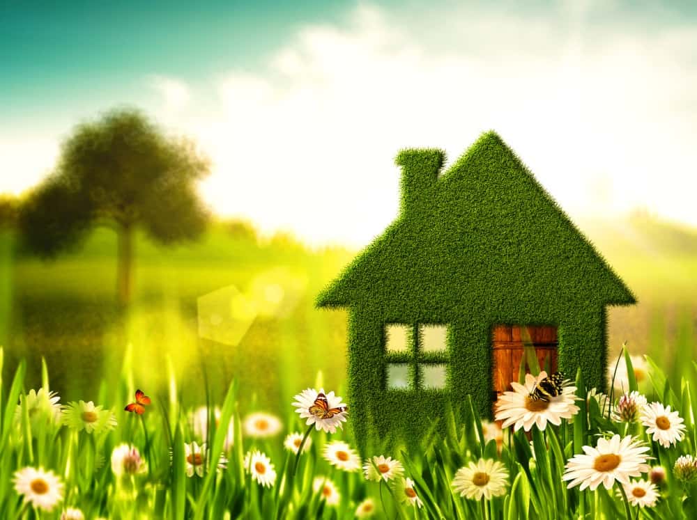 Symbolisches grünes Haus aus Gras in einer blühenden Frühlingswiese – steht für Nachhaltigkeit, Umweltbewusstsein und ökologisches Bauen.