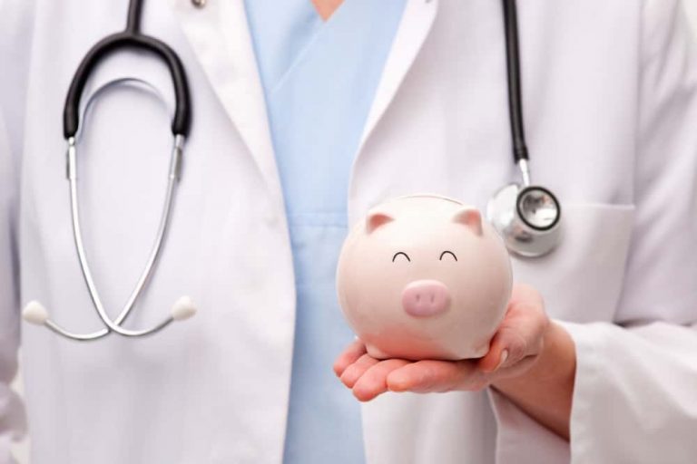 Ein Arzt in weißem Kittel und mit Stethoskop hält ein Sparschwein in der Hand. Das Sparschwein hat ein lächelndes Gesicht. Dies symbolisiert Verbindung zwischen Gesundheit und Finanzen.