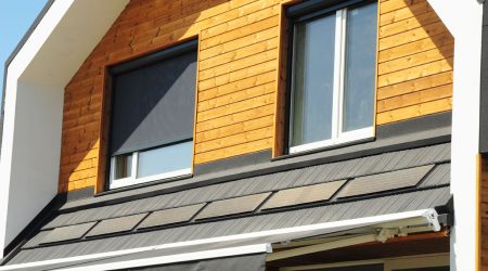 Modernes Einfamilienhaus mit Holzfassade und Fenstern, ausgestattet mit elektrisch betriebenen Rollläden, die über ein Smart-Home-System gesteuert werden.