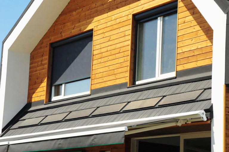Modernes Einfamilienhaus mit Holzfassade und Fenstern, ausgestattet mit elektrisch betriebenen Rollläden, die über ein Smart-Home-System gesteuert werden.