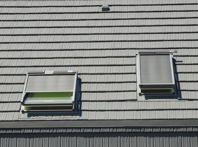 Zwei Dachfenster mit integrierten, elektrisch betriebenen Rollläden, steuerbar über ein Smart-Home-System, installiert auf einem modernen Ziegeldach.