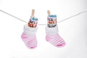 Zwei kleine, rosa-weiße Babysocken hängen an einer Wäscheleine und sind jeweils mit mehreren Euro-Geldscheinen gefüllt. Symbolisch für Kinderfreibetrag.
