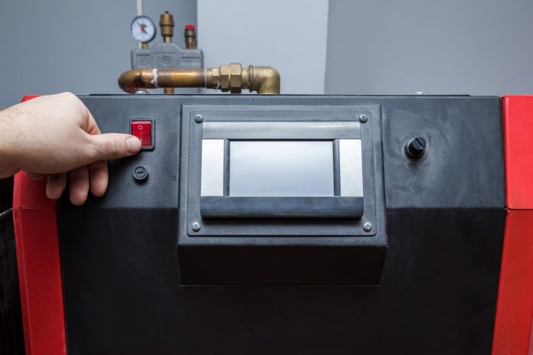 Hand drückt auf den Piezozünder eines Gasheizgeräts mit Display zur manuellen Zündung durch Zündfunken.