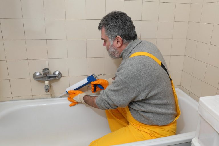 Sanitärinstallateur mit gelber Hose verfugt eine Badewanne neu