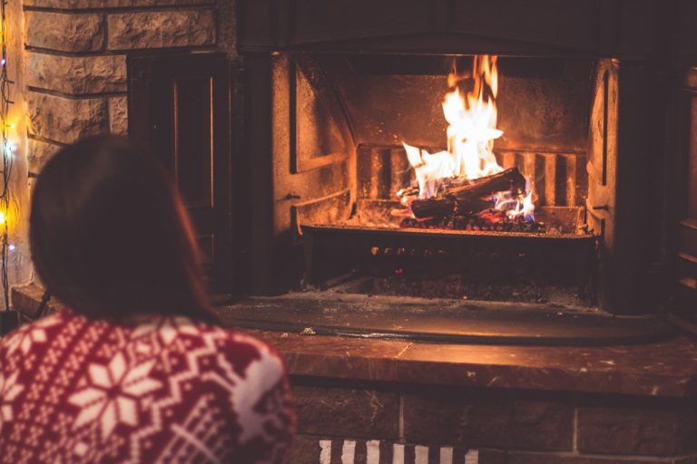 Frau sitzt vor Kamin mit Feuer.