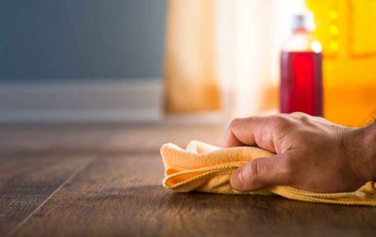 Hand mit Lappen wischt über Laminat