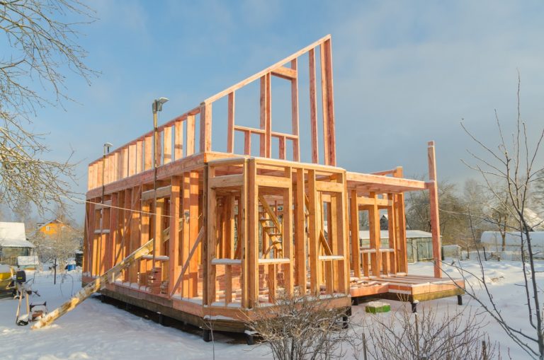 Haus im Rohbau mit Holzständerwerk auf verschneitem Grundstück – Winterbauphase eines Holzhauses im Rahmenbauverfahren.