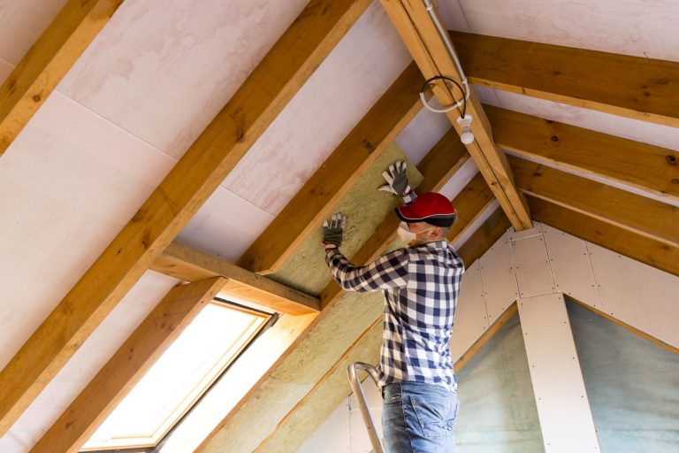 Handwerker bringt Dachdämmung am Dachboden an
