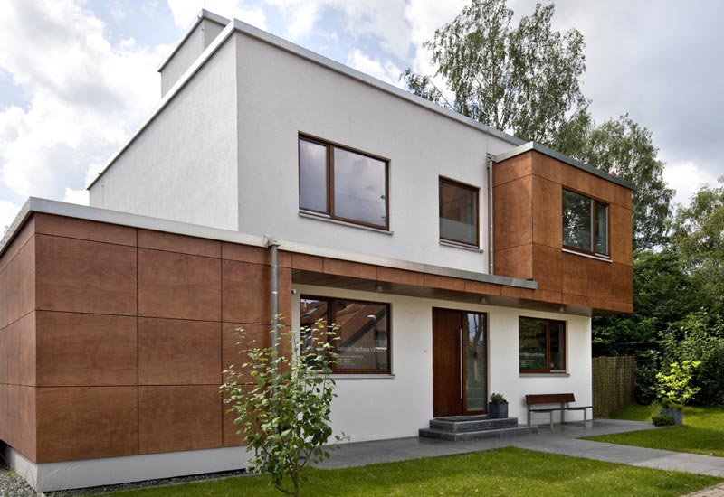 Moderner Anbau an einem Bestandsgebäude mit Flachdach und Holzpaneelen – Kombination aus weißem Putz und natürlicher Holzoptik. Ein Beispielhaus eines Holzrahmenbaus der Firma Puschmann Architektur.
