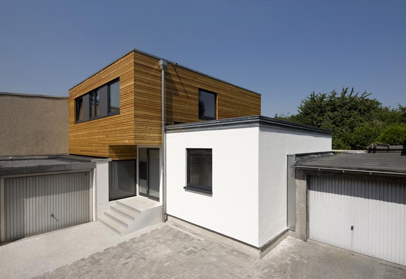 Moderner Hausanbau mit Holzfassade im Obergeschoss und weiß verputztem Erdgeschoss – Verbindung von Alt- und Neubau mit Flachdacharchitektur. Ein Beispielhaus eines Holzrahmenbaus der Firma Puschmann Architektur.