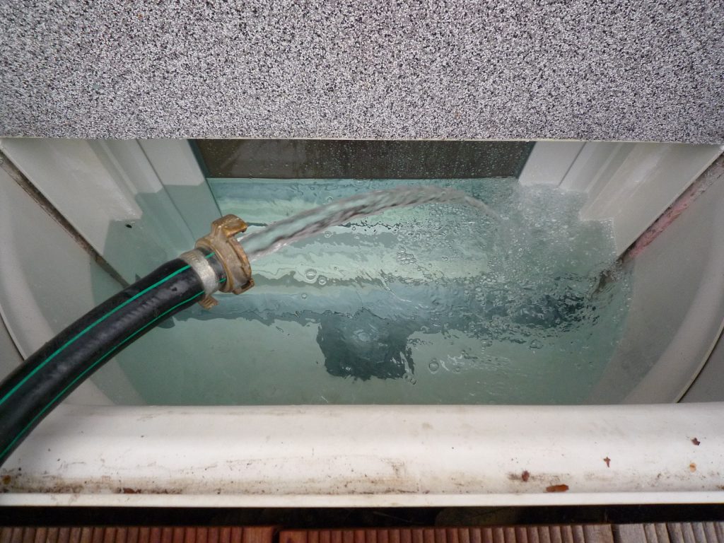Wasserdichtes Kellerfenster wird mit Wasserschlauch zum Test mit Wasser befüllt