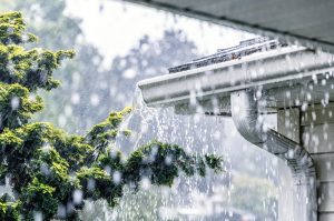 Starker Regen fließt über eine verstopfte Dachrinne, Wasser läuft unkontrolliert über den Dachrand.