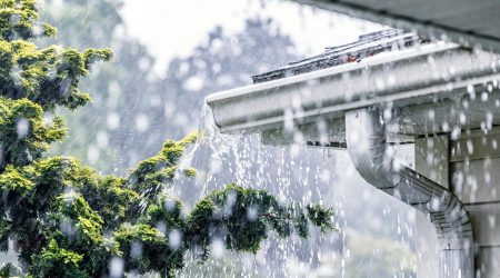 Starker Regen fließt über eine verstopfte Dachrinne, Wasser läuft unkontrolliert über den Dachrand.