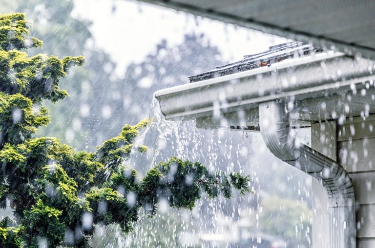 Starker Regen fließt über eine verstopfte Dachrinne, Wasser läuft unkontrolliert über den Dachrand.