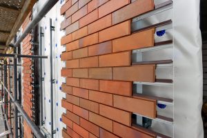 Montage einer vorgehängten hinterlüfteten Fassade mit keramischen Klinkerriemchen auf Aluminiumunterkonstruktion, sichtbar auf einer eingerüsteten Baustelle.
