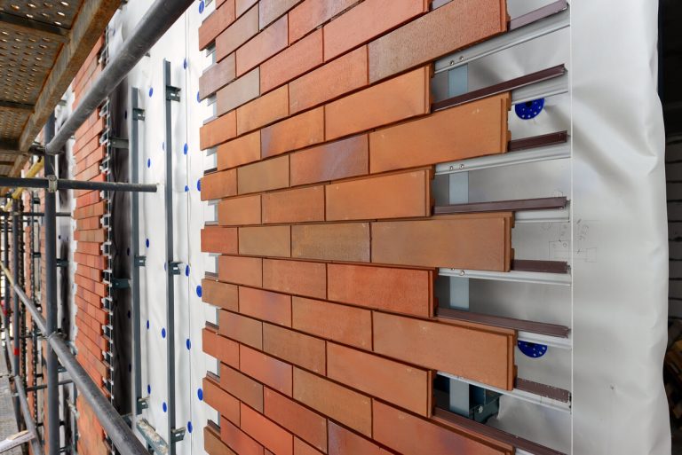 Montage einer vorgehängten hinterlüfteten Fassade mit keramischen Klinkerriemchen auf Aluminiumunterkonstruktion, sichtbar auf einer eingerüsteten Baustelle.