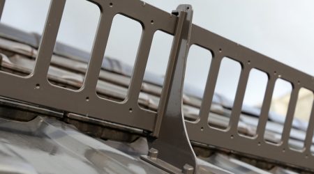 Nahaufnahme eines Schneefanggitters aus Metall, das auf einem geneigten Metalldach montiert ist. Das System dient zur Verhinderung von abrutschendem Schnee.