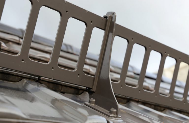 Nahaufnahme eines Schneefanggitters aus Metall, das auf einem geneigten Metalldach montiert ist. Das System dient zur Verhinderung von abrutschendem Schnee.
