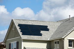 Einfamilienhaus mit hellgrauem Ziegeldach, in das flächenbündig schwarze Solarziegel integriert sind, bei leicht bewölktem Himmel.