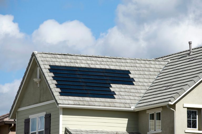 Einfamilienhaus mit hellgrauem Ziegeldach, in das flächenbündig schwarze Solarziegel integriert sind, bei leicht bewölktem Himmel.