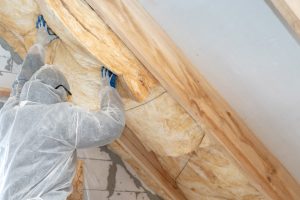 Handwerker in Schutzanzug bringt Dämmstoff der Zwischensparrendämmung an