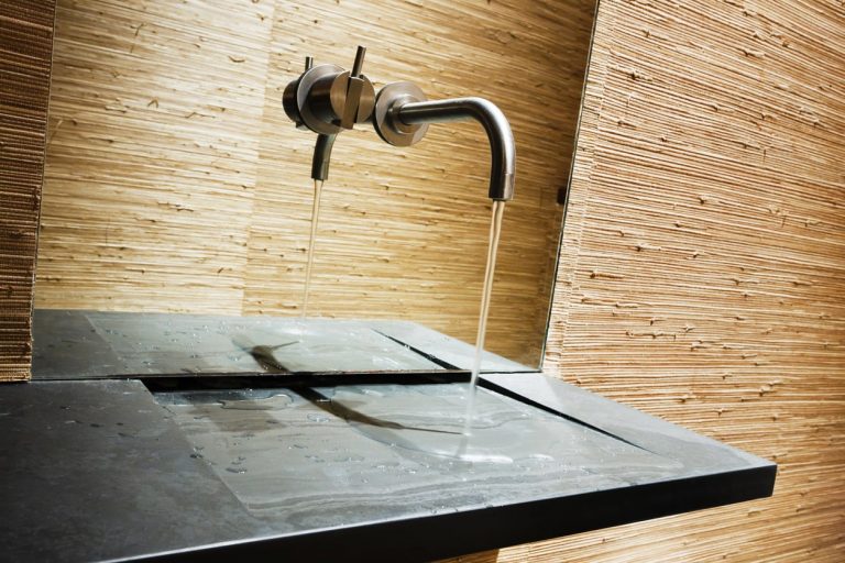 Dunkles Waschbecken aus Naturstein mit laufendem Wasser an einer hellen Wand