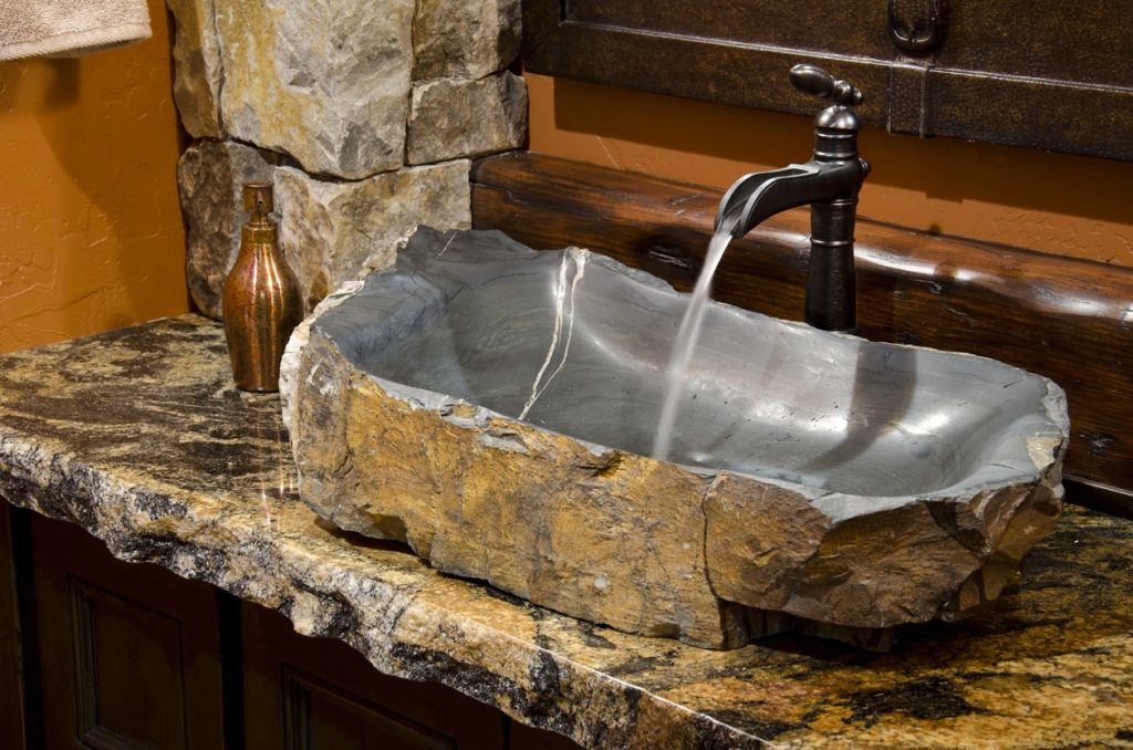 Waschbecken in einem Badezimmer aus dunklem Naturstein mit laufendem Wasserhahn