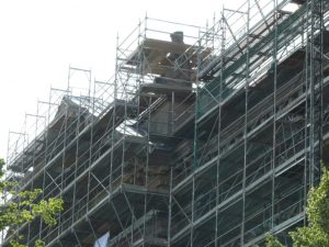 Großflächiges Fassadengerüst mit integrierten Dachfanggittern und Schutznetzen an einem mehrstöckigen Gebäude in Sanierung.