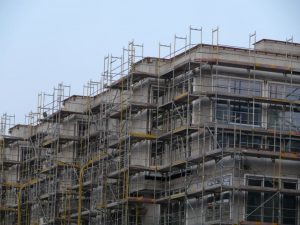 Großflächiges Fassadengerüst mit integrierter Dachrandsicherung an einem mehrstöckigen Gebäude während der Bauphase.