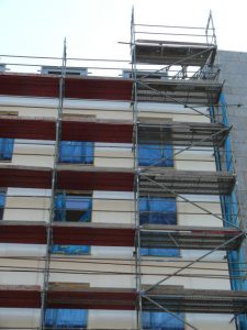 Fassadengerüst an einem mehrstöckigen Wohngebäude mit roten Gerüstbelägen und gesicherten Arbeitsbühnen für Sanierungsarbeiten.