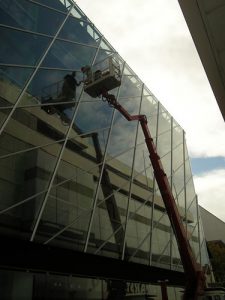 Arbeiter auf einer Hubarbeitsbühne bei der Glasreinigung einer modernen Fassadenverkleidung aus Glas an einem Bürogebäude.