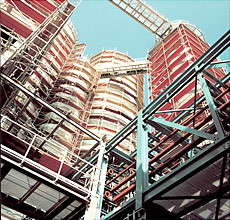 Industriegerüst mit umlaufenden Arbeitsplattformen an zylindrischen Behältern auf einem Werksgelände unter freiem Himmel.