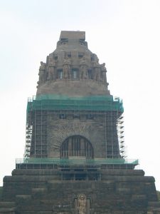 Denkmal mit Sondergerüst während Sanierungsarbeiten, frontale Ansicht mit Figuren und großem Torbogen aus Stein.