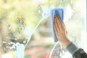Frauenhand wischt mit einem Mikrofastertuch über eine Fensterscheibe