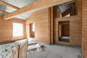 Innenansicht eines im Bau befindlichen Holzhauses mit sichtbarer Dämmung im Dachbereich und offenem Grundriss.