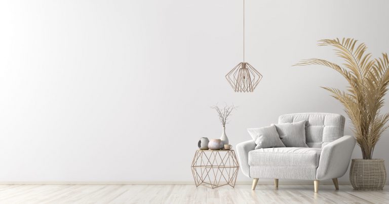 Helles, minimalistisches Wohnzimmer mit grauem Polstersessel, zwei Kissen, geometrischem Couchtisch und hängender Lampe. Neben dem Tisch stehen kleine Vasen und eine getrocknete Pflanze. Rechts steht eine große, getrocknete Palme in einem Korb.