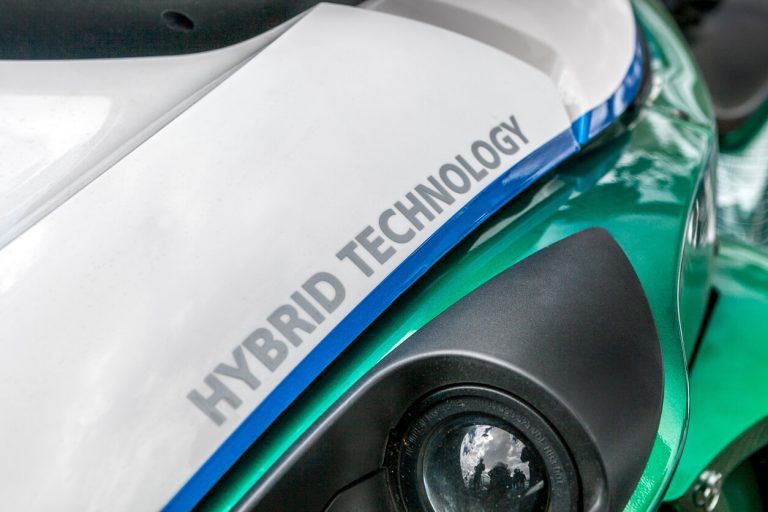 Detailaufnahme eines Fahrzeugs mit der Aufschrift "Hybrid Technology" auf der Motorhaube, grün-weiß lackiert, mit Fokus auf das Scheinwerferdesign und die umweltfreundliche Antriebstechnologie.