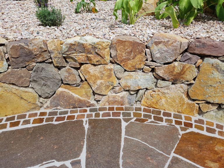 Natursteinmauer aus verschiedenfarbigen Bruchsteinen mit angrenzendem Bodenbelag aus polygonalem Natursteinpflaster – ideal für mediterrane Gartengestaltung.