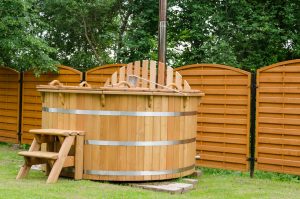 Holzbefeuerter Hot Tub aus Holz im Garten, mit Holztreppe und Sichtschutzwand im Hintergrund.