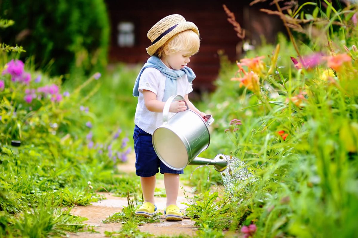 Kleines Kind mit Gießkanne im Garten.