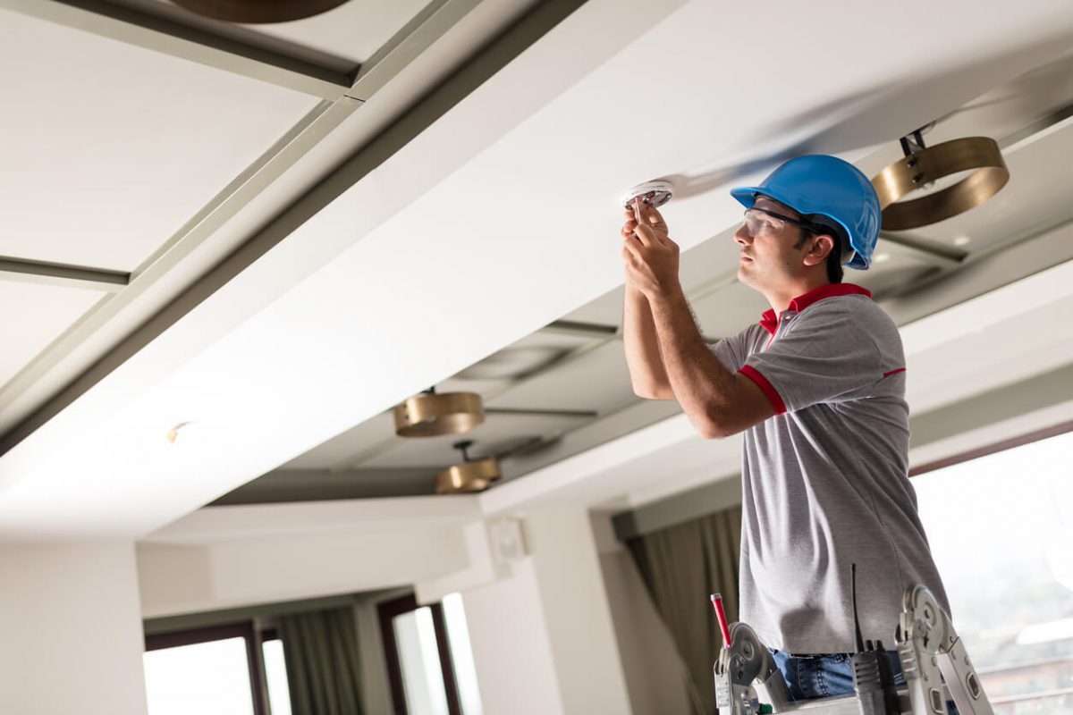 Handwerker wechselt einen Brandmelder aus.