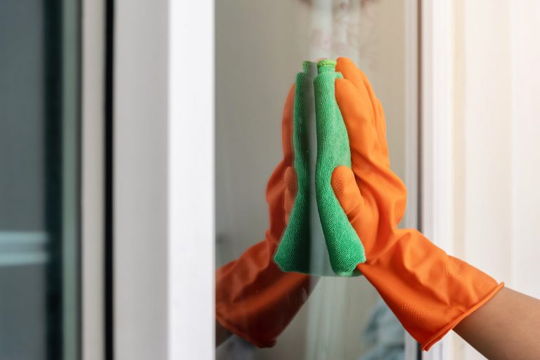 Hand mit Schutzhandschuh wischt mit einem Tuch über eine Glasscheibe.